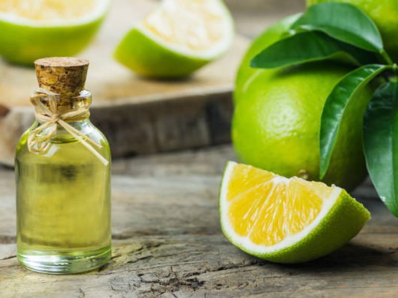 Glass bottle of lemon essential oil and fresh green lemons on wooden rustic background, alternative medicine aromatherapy and Spa concept